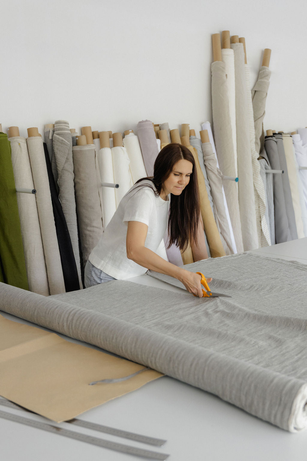 Woman cutting linen fabric in a room with various linen fabric rolls.
