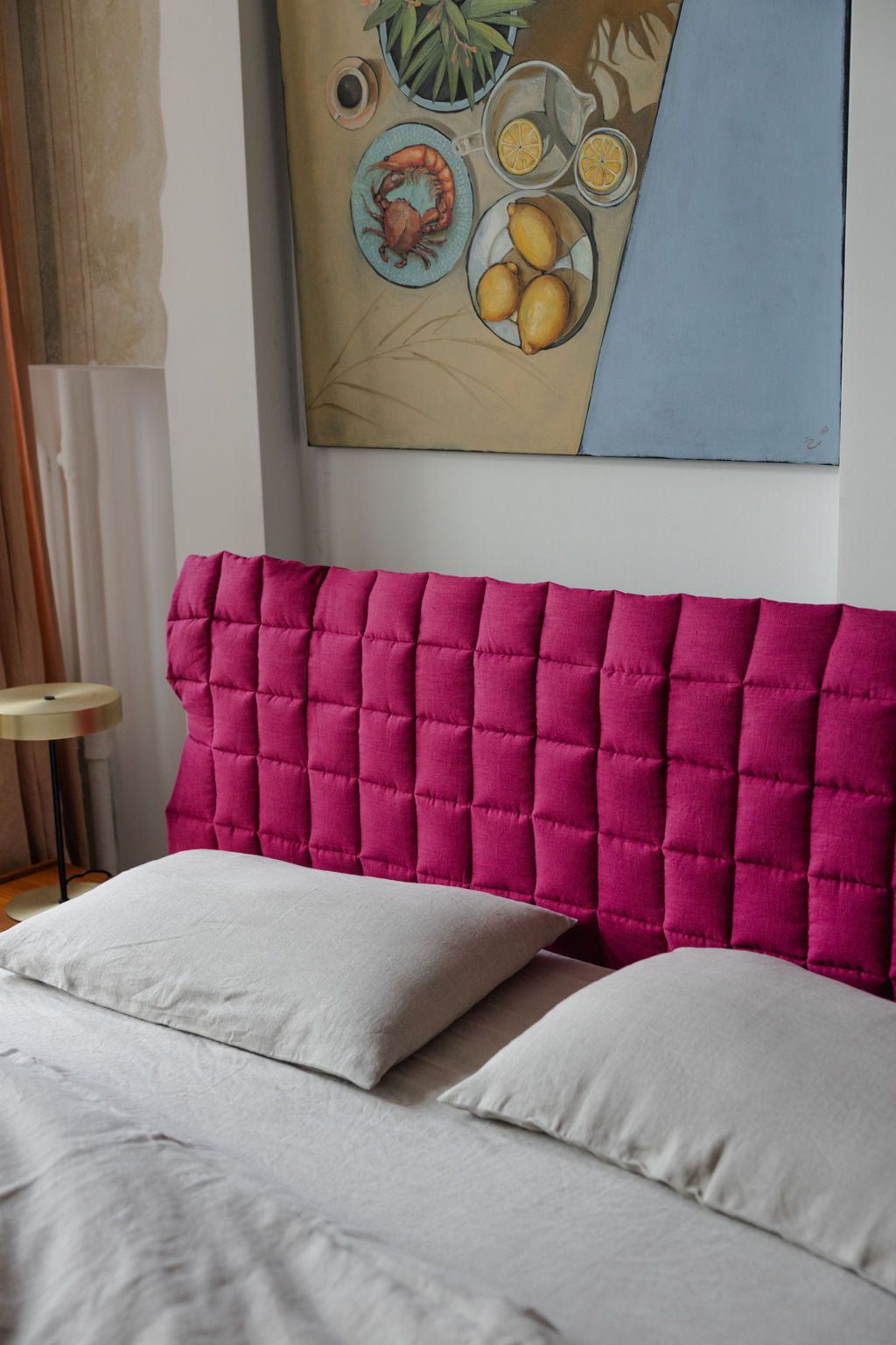 Bedroom with a pink quilted headboard and a painting on the wall.