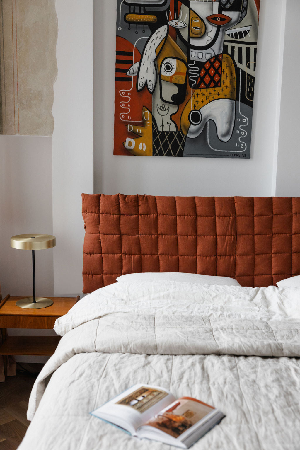 Bedroom with a red quilted headboard, white bedding, and a colorful abstract painting on the wall.