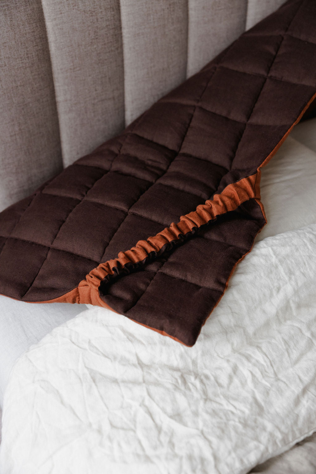 Brown quilted blanket with orange trim on a bed