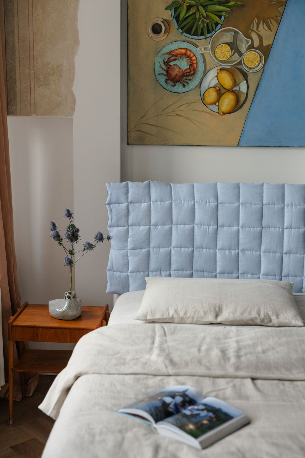 Bedroom with a light blue upholstered headboard and a painting on the wall.
