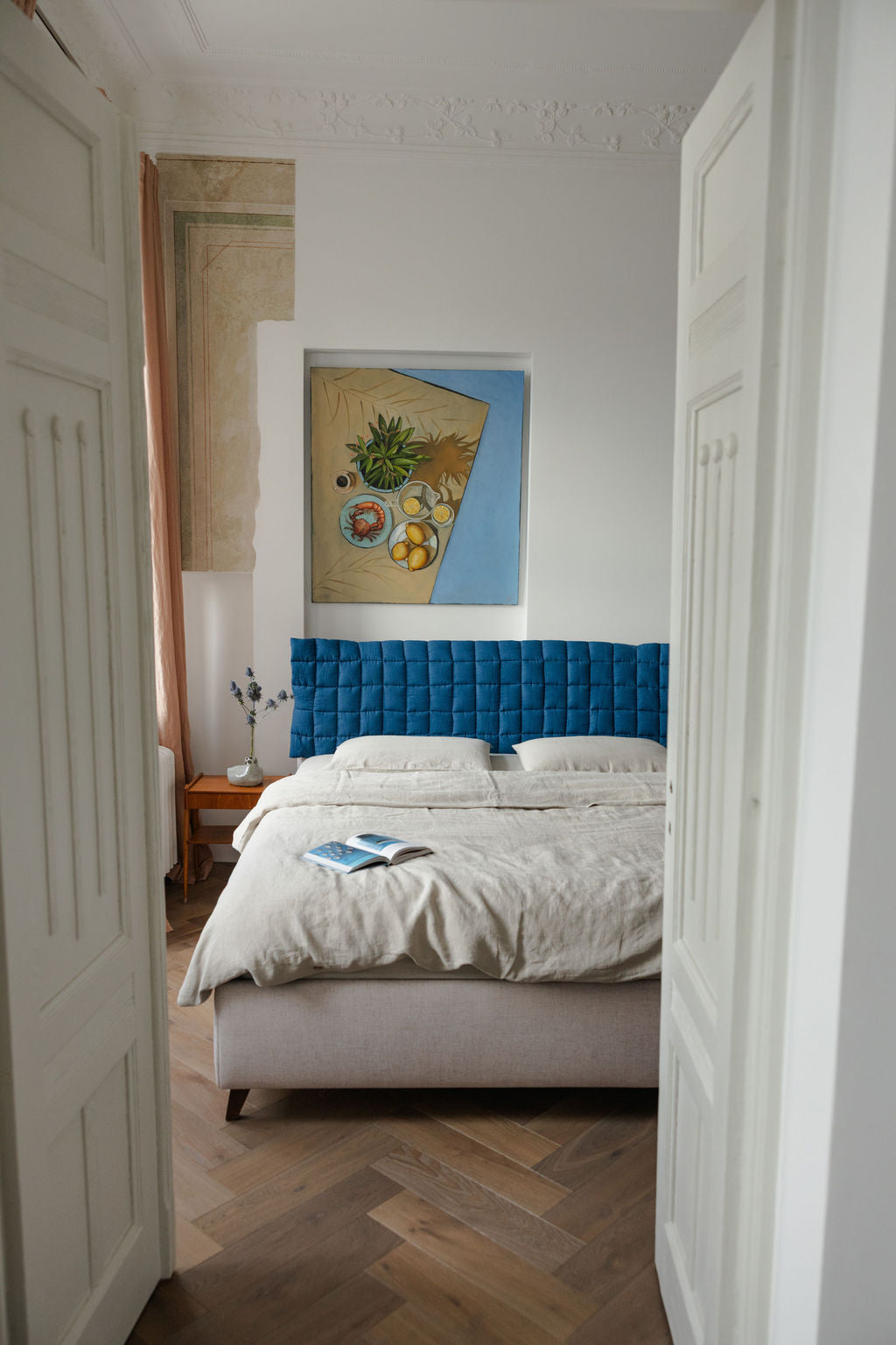 Bedroom with a blue tufted headboard and white bedding, featuring a painting on the wall.