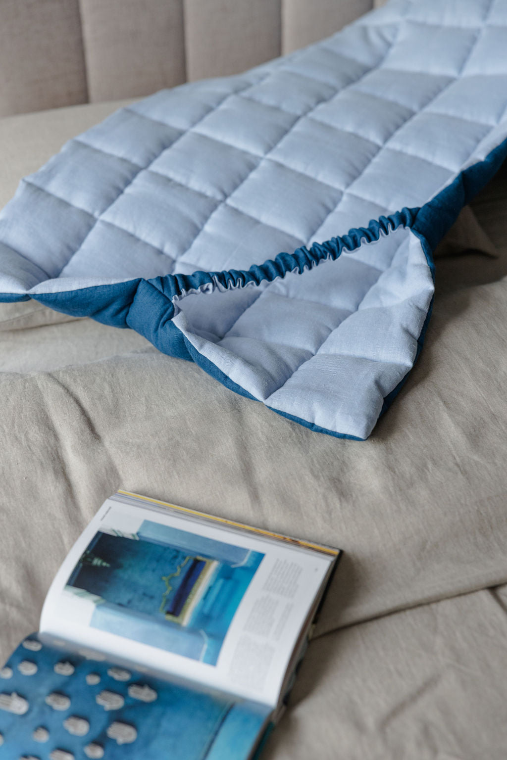 Blue quilted cover on a beige bed with an open book underneath