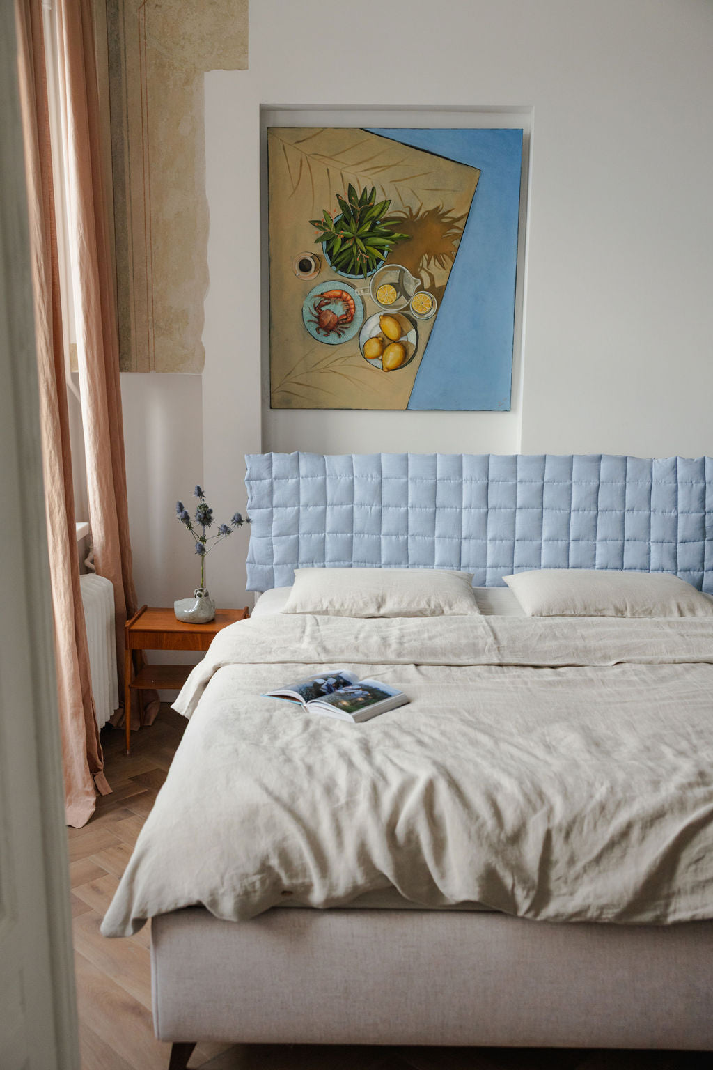Bedroom with a light blue upholstered headboard and a painting on the wall.