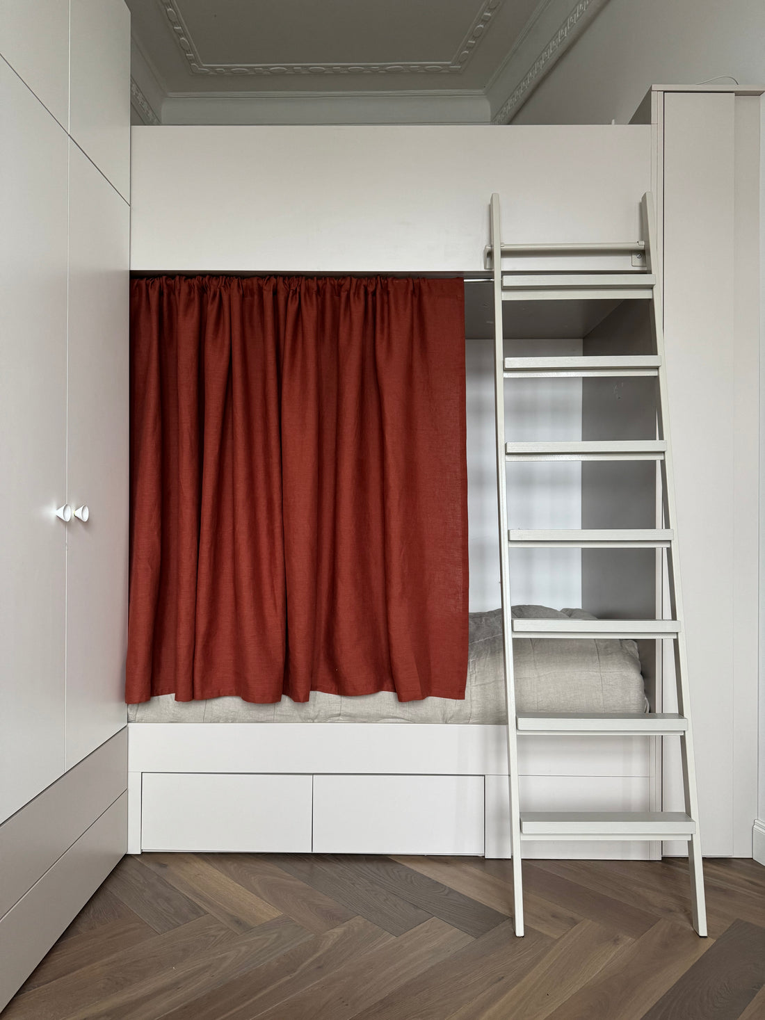 Small bedroom with a bunk bed, ladder, and rust linen curtain.
