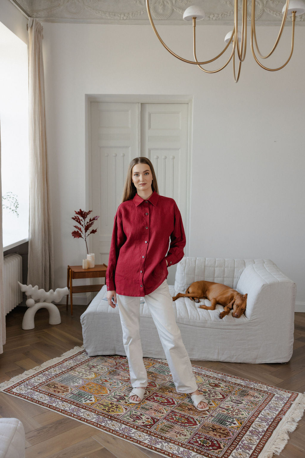 Woman in a red shirt standing in a living room with a dog on a couch.