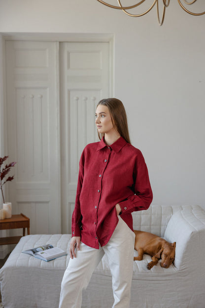 Woman in a red shirt and white pants standing in a room with a dog on a bed.