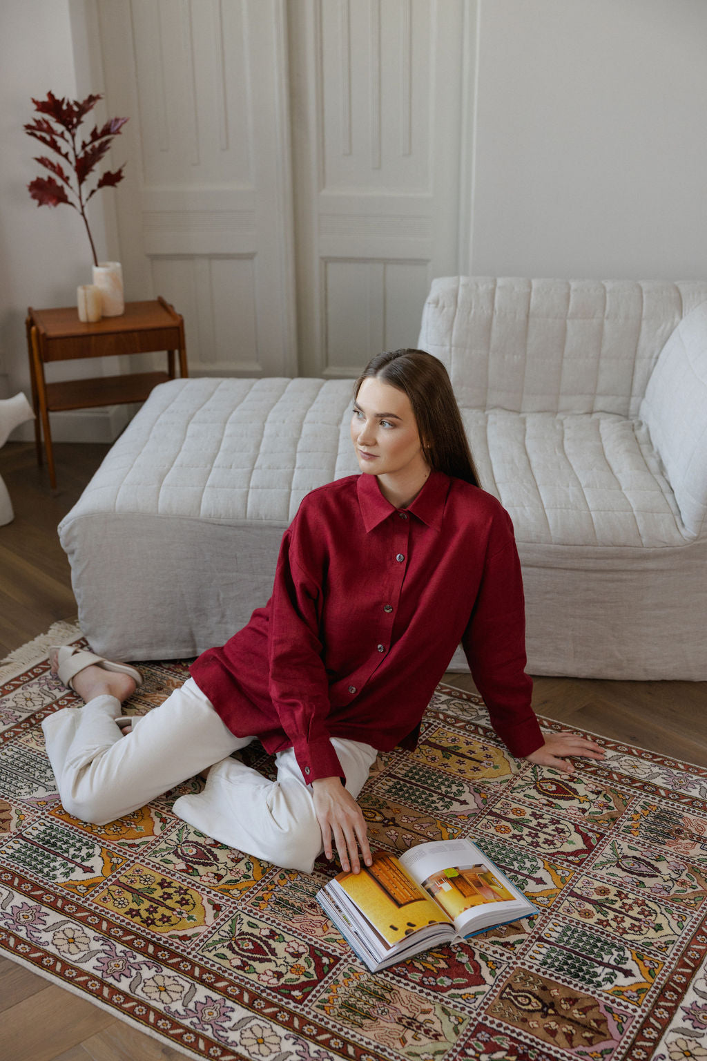 Woman in a red shirt sitting on a patterned rug with an open book