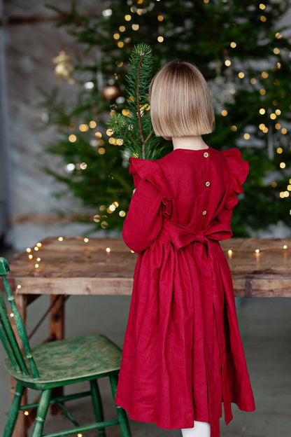 Young girl in a red dress holding a Christmas tree branch in front of a decorated Christmas tree.