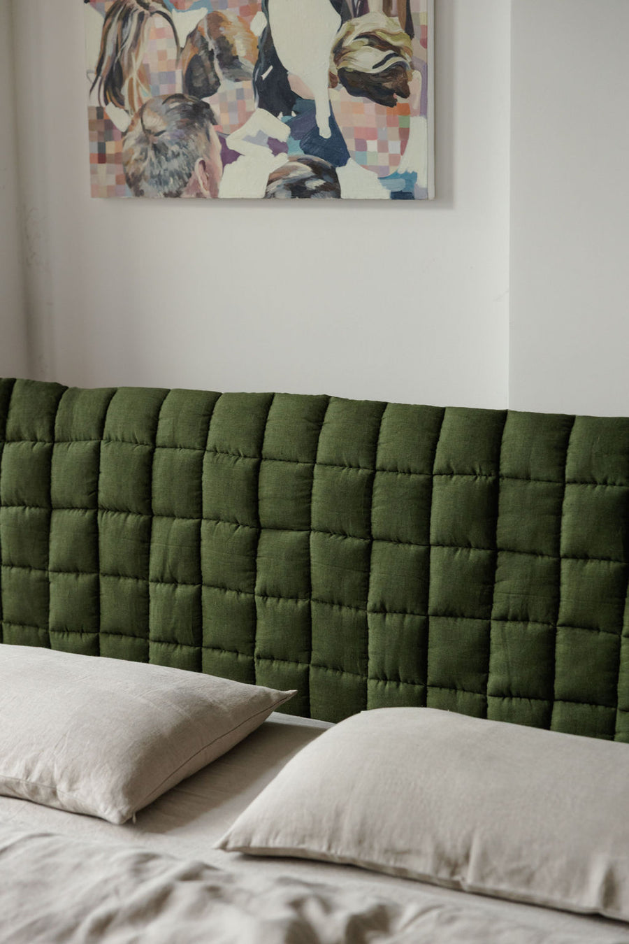 Green quilted headboard with pillows and a colorful abstract painting on the wall.