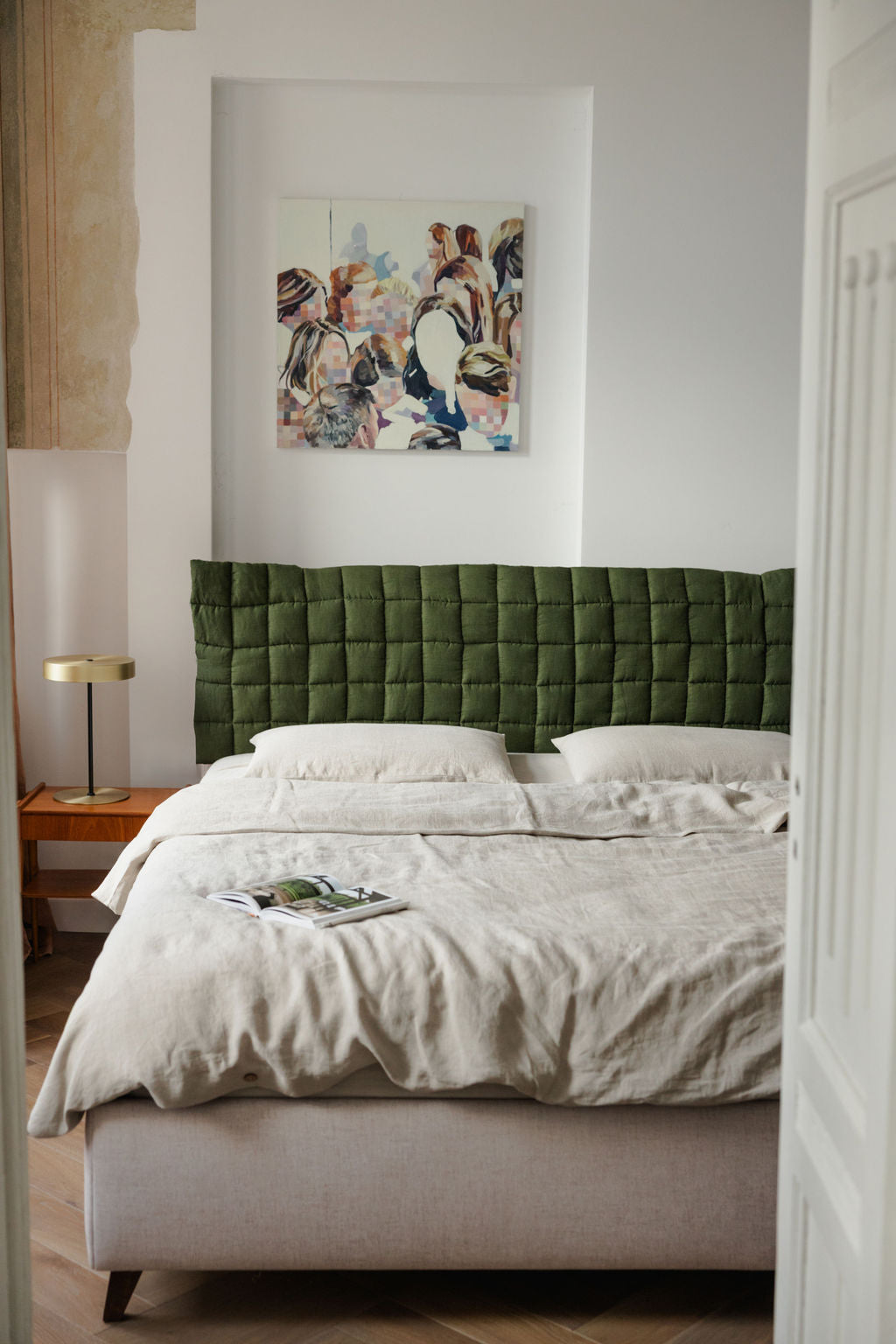 Bedroom with a green upholstered headboard and abstract painting on the wall.