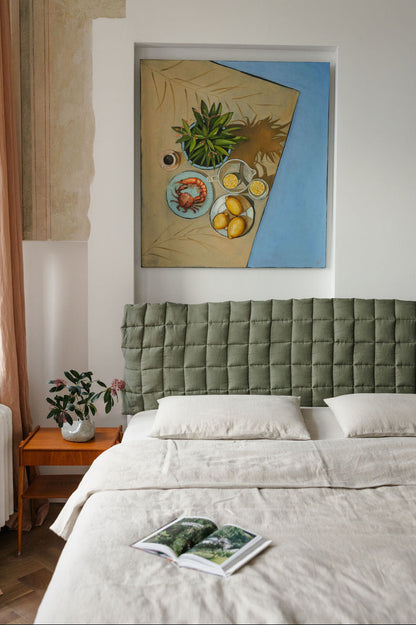 Bedroom with green headboard, framed artwork on wall, and small table with plant.