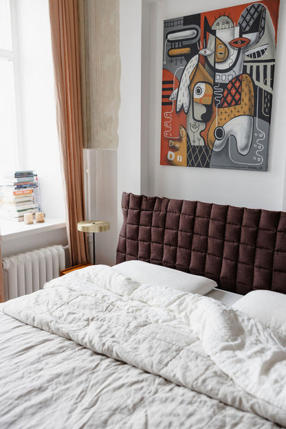 Bedroom with a brown quilted headboard, white bedding, and abstract artwork on the wall.