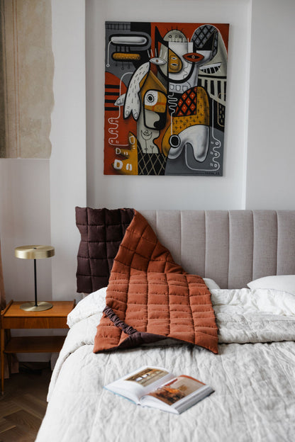 Bedroom with a bed featuring a quilt and pillows, a nightstand with a lamp, and a colorful abstract painting on the wall.