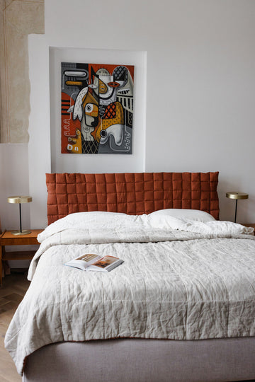 Bedroom with a red quilted headboard and abstract art on the wall.