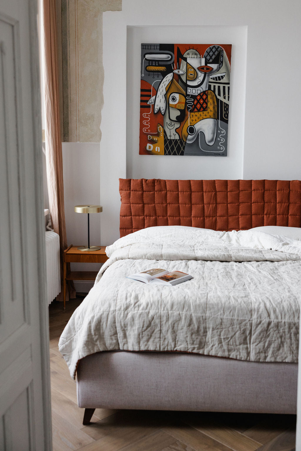 Bedroom with a bed featuring a textured headboard, white bedding, and a colorful abstract painting on the wall.