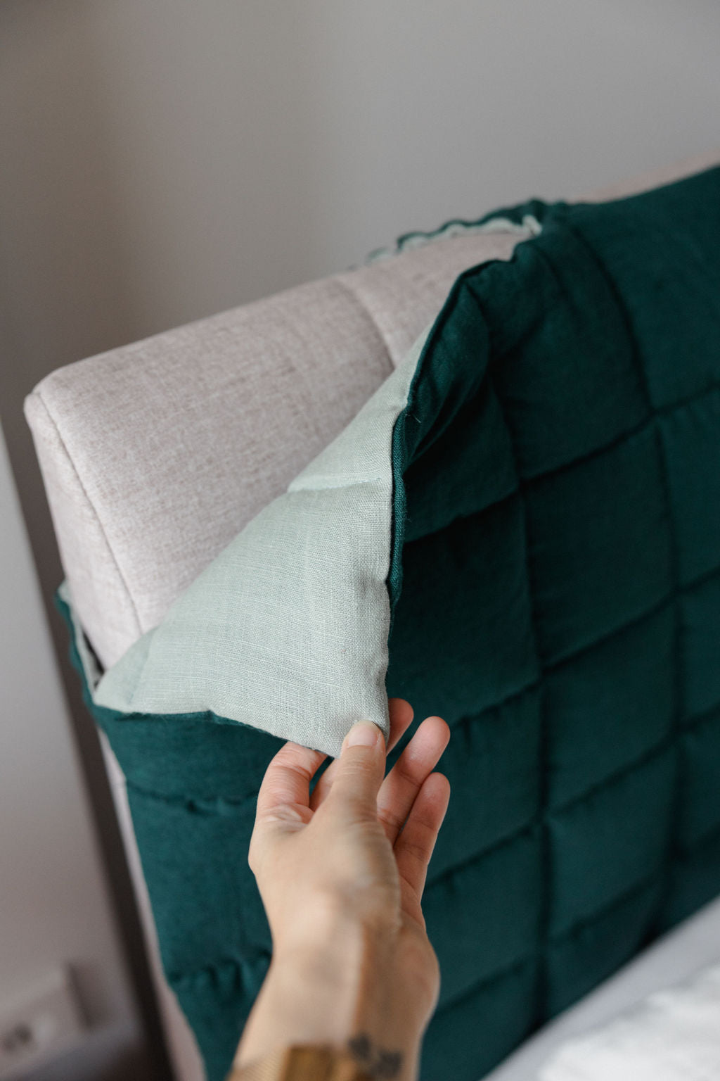 Person adjusting a green quilted pillow on a bed