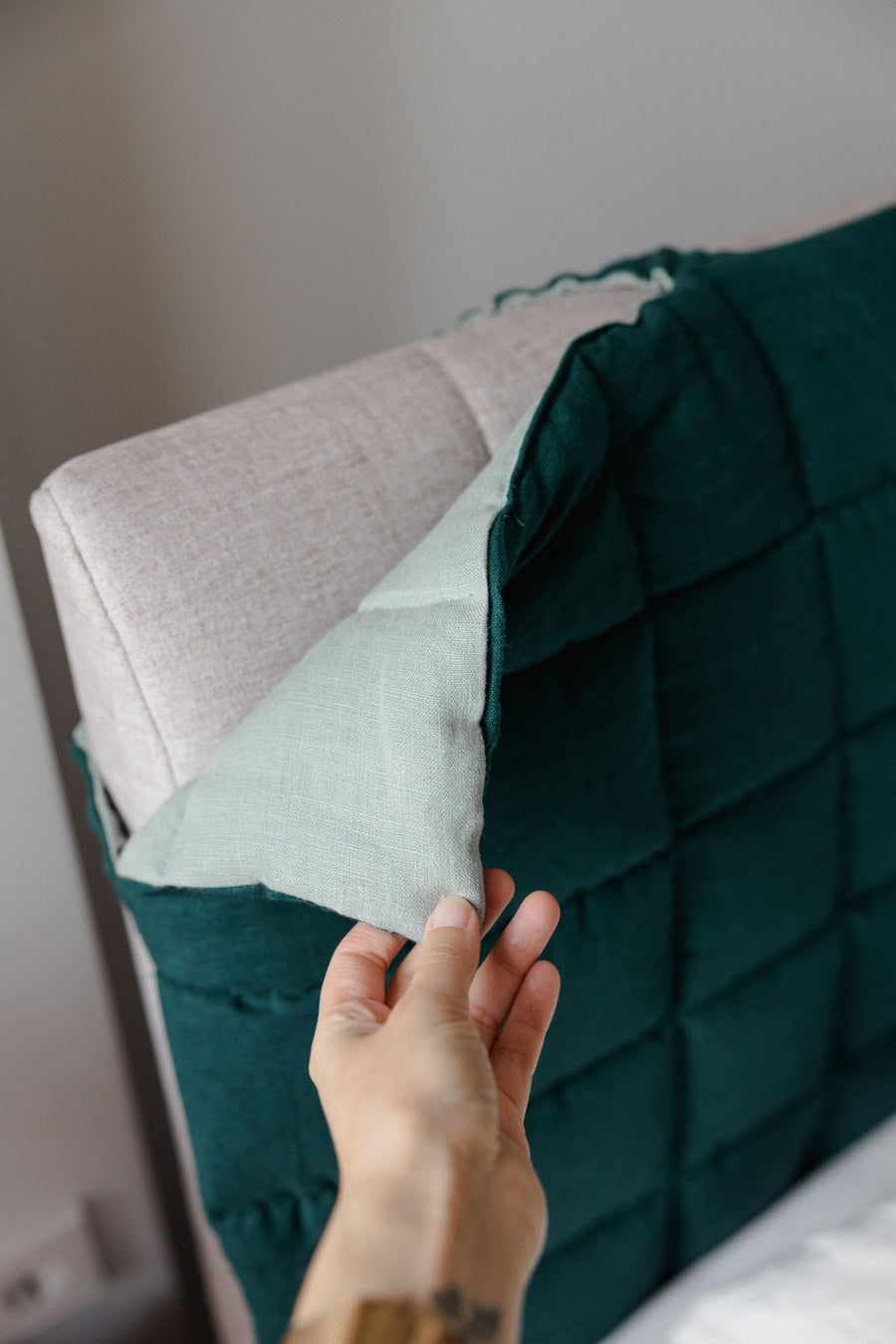 Person adjusting a green quilted pillow on a bed