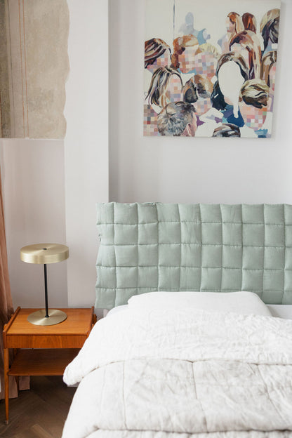 Bedroom with a green headboard, white bedding, and a nightstand with a lamp.