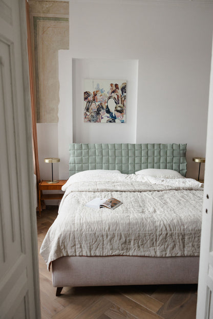 Neatly made bed in a bedroom with a light green headboard and decorative wall art.