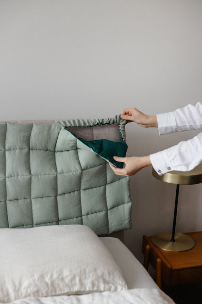 Person adjusting a green pillow on a bed with a neutral background