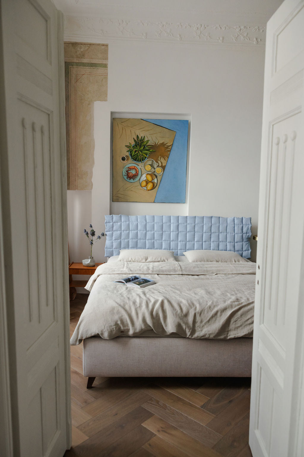 Bedroom with a light blue tufted headboard and a painting on the wall.