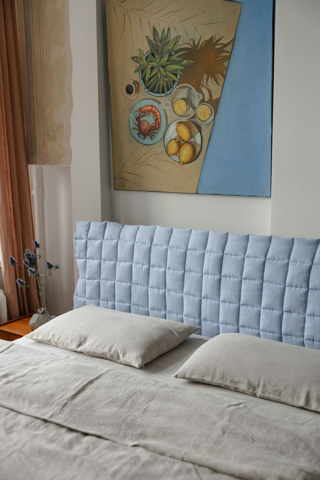 Bedroom with a light blue quilted headboard and a painting on the wall.