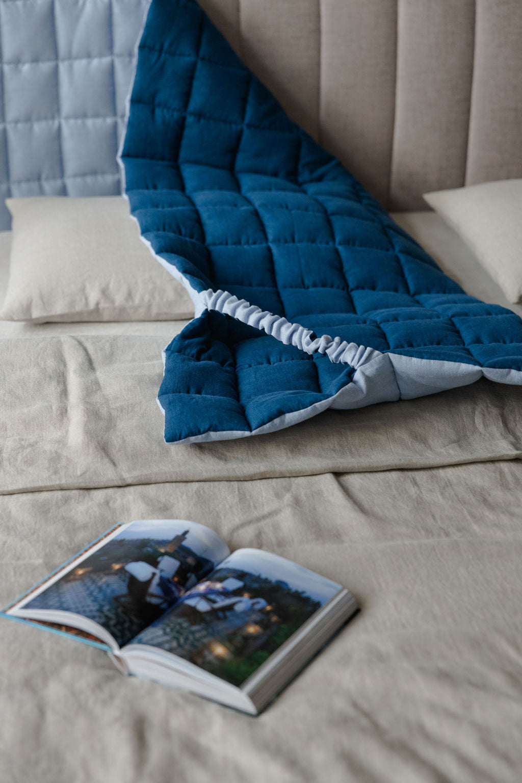 Blue quilt draped over a bed with an open book on a nightstand.