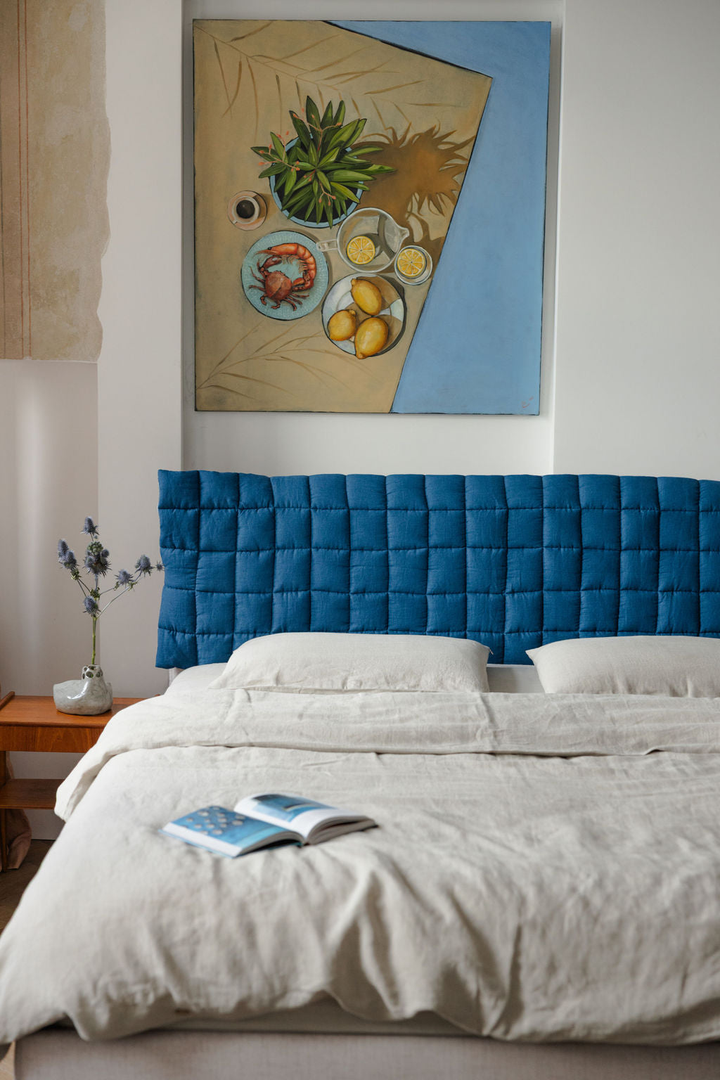 Bedroom with a blue upholstered headboard and a painting on the wall.