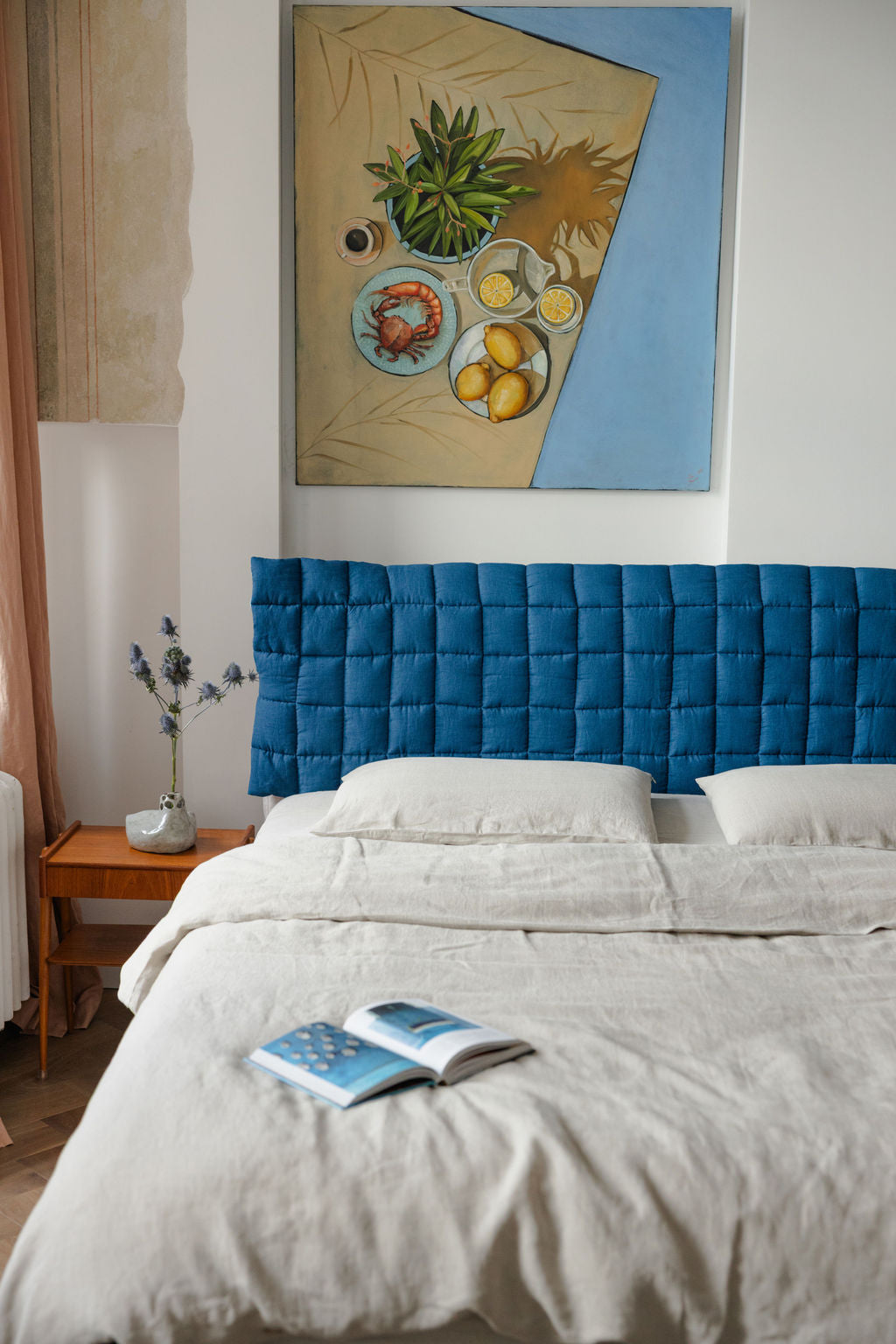 Bedroom with a blue upholstered headboard and a painting on the wall.