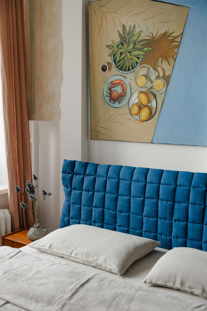 Bedroom with a blue tufted headboard and artwork on the wall.