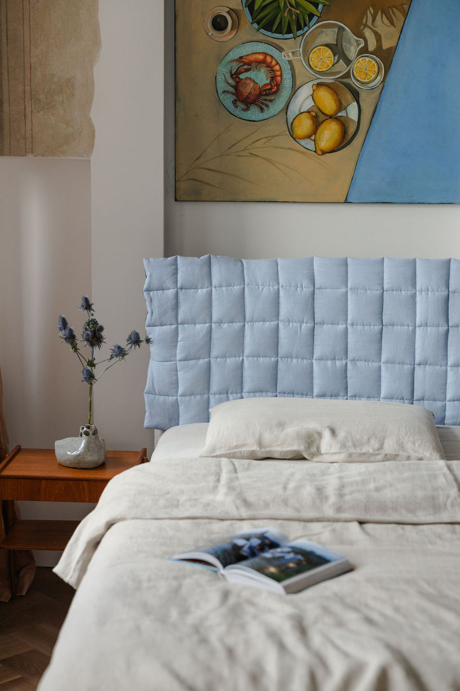 Bedroom with a light blue quilted headboard and a painting on the wall.