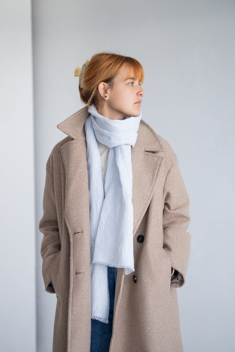 Person wearing light blue linen scarf against a plain background

