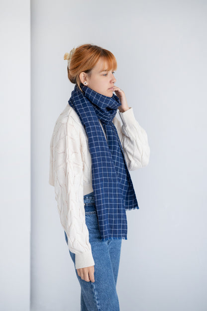 Person wearing blue linen checkered scarf against a plain background
