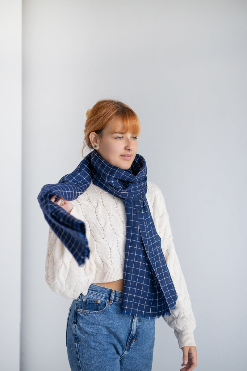 Woman wearing a blue checkered linen scarf and white sweater against a gray background
