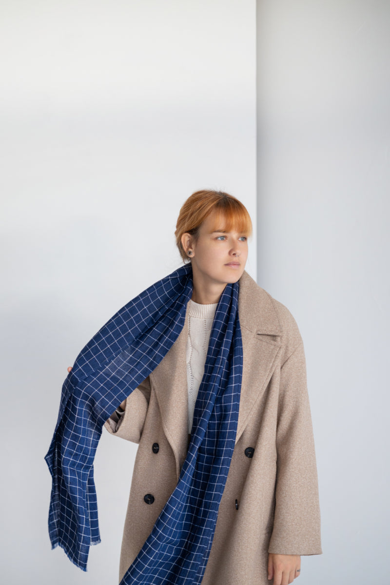 Person wearing blue gingham linen scarf against a plain background